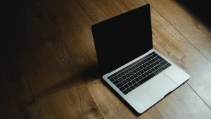 MacBook placed diagonally on a warm wooden floor with soft lighting.